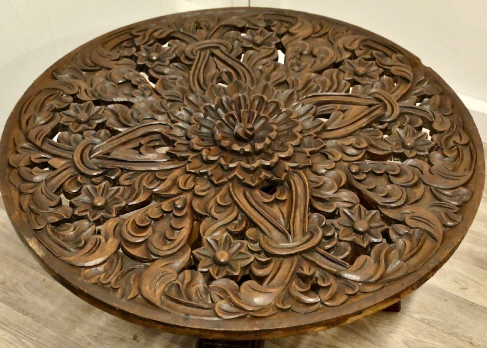 A low circular coffee table made of dark walnut wood featuring a glass top surface, a heavy turned pedestal baluster, and a four-star carved base. View VIII