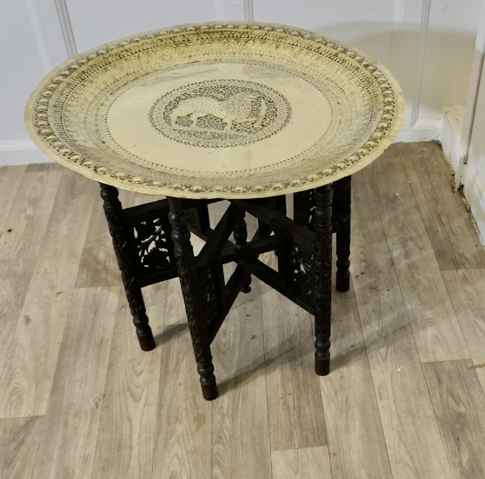 An Anglo-Indian occasional table featuring a circular hand-engraved brass tray resting on a dark carved folding wooden base. View II