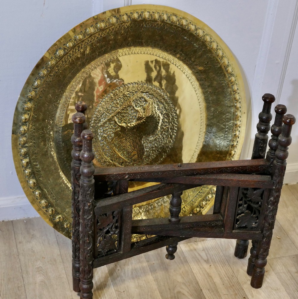 An Anglo-Indian occasional table featuring a circular hand-engraved brass tray resting on a dark carved folding wooden base. View V