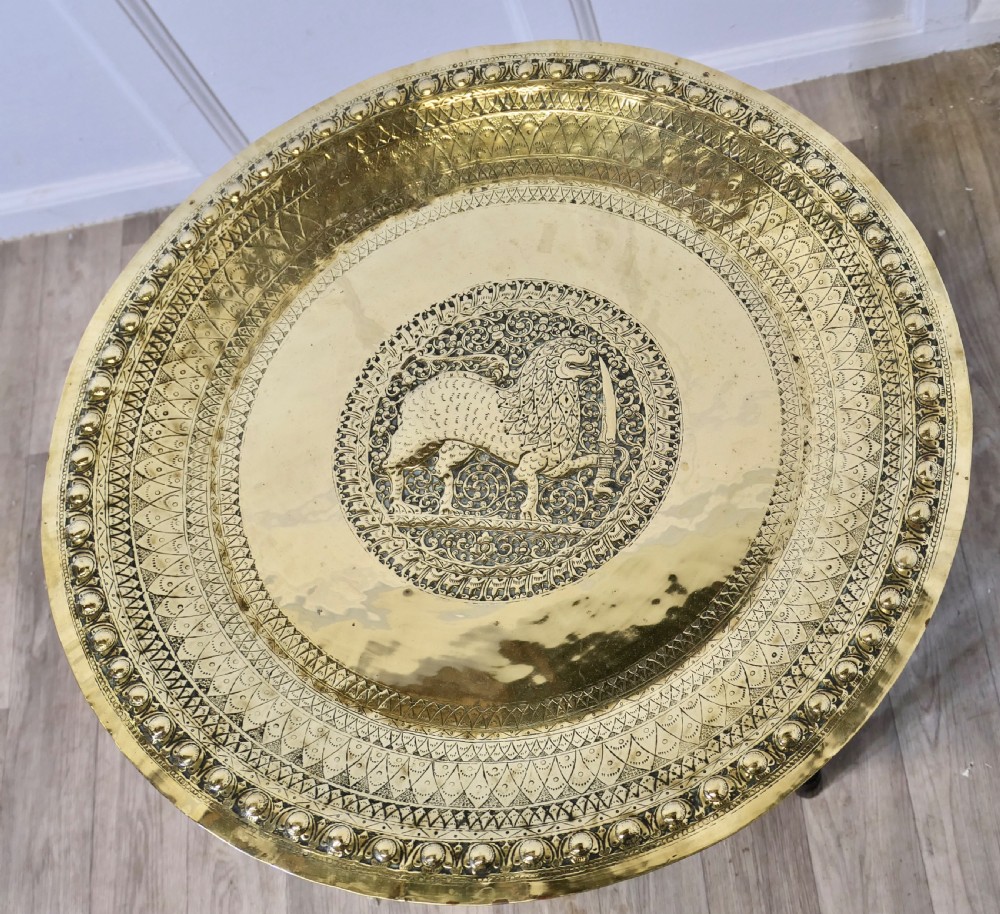 An Anglo-Indian occasional table featuring a circular hand-engraved brass tray resting on a dark carved folding wooden base. View VI