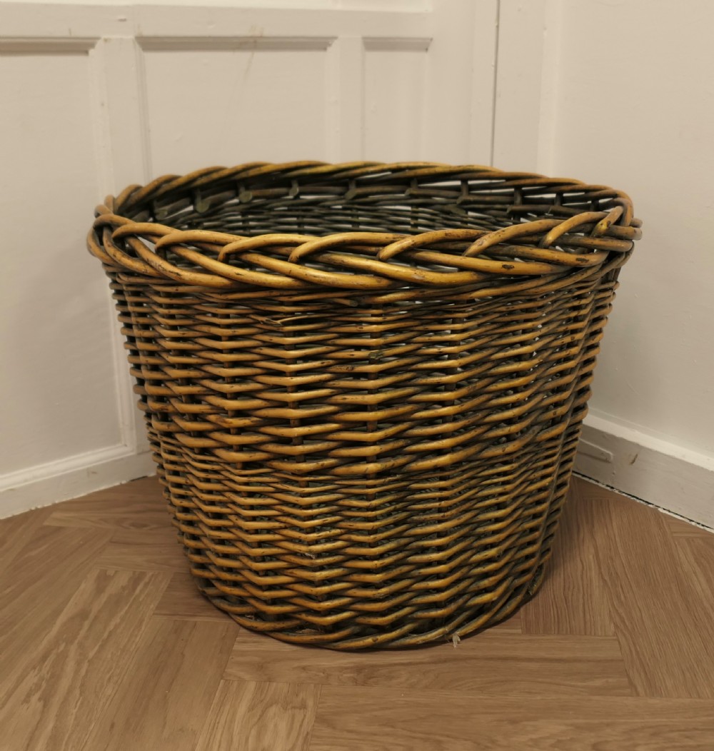 A large circular woven willow log basket with a braided rim resting on a wooden floor.