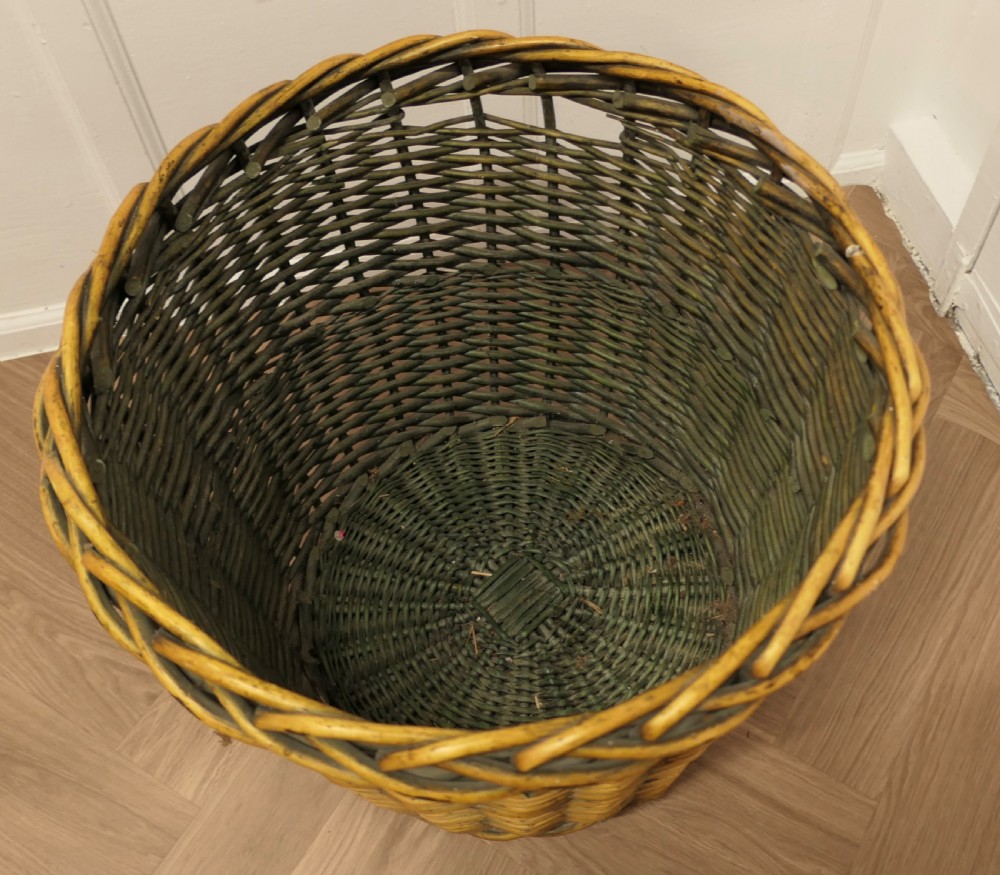 A large circular woven willow log basket with a braided rim resting on a wooden floor. View V