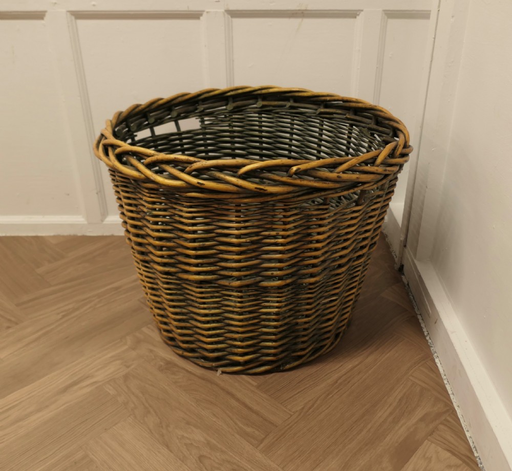 A large circular woven willow log basket with a braided rim resting on a wooden floor. View VI