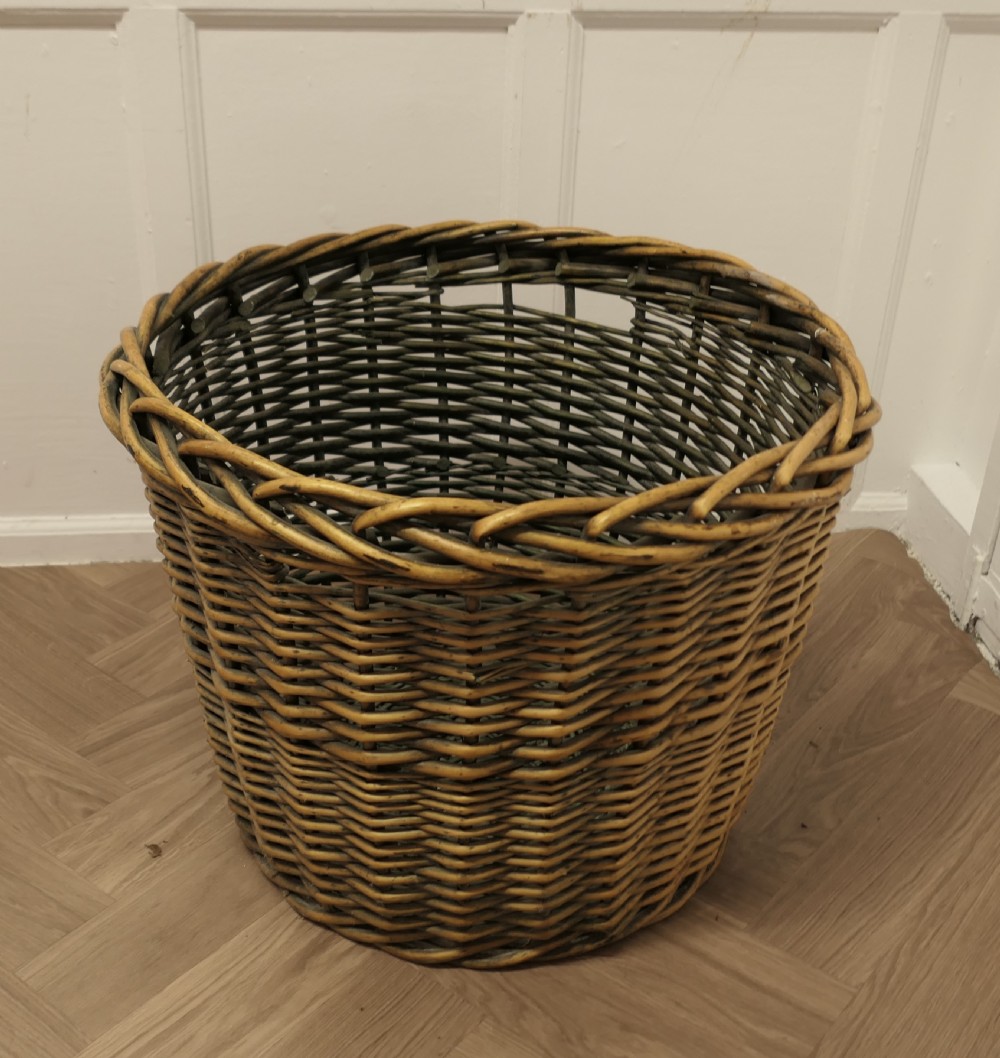 A large circular woven willow log basket with a braided rim resting on a wooden floor. View VII