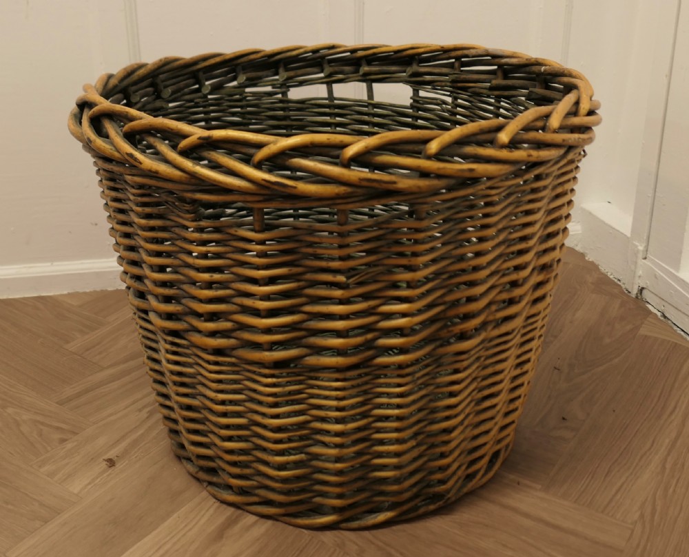 A large circular woven willow log basket with a braided rim resting on a wooden floor. View VIII