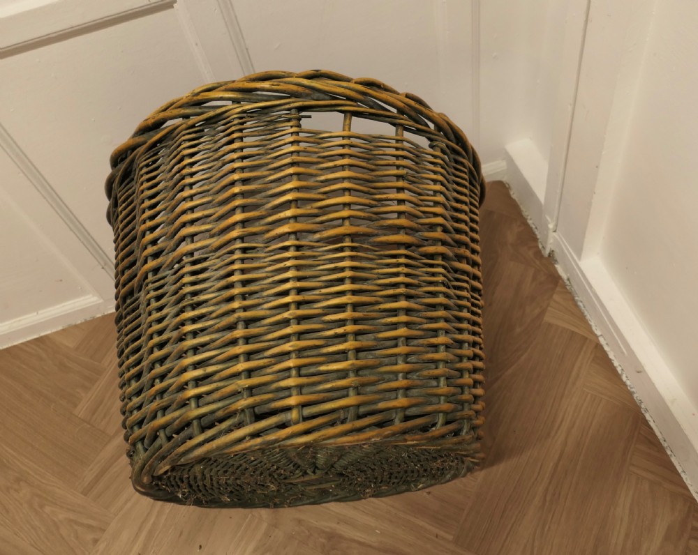 A large circular woven willow log basket with a braided rim resting on a wooden floor. View IX