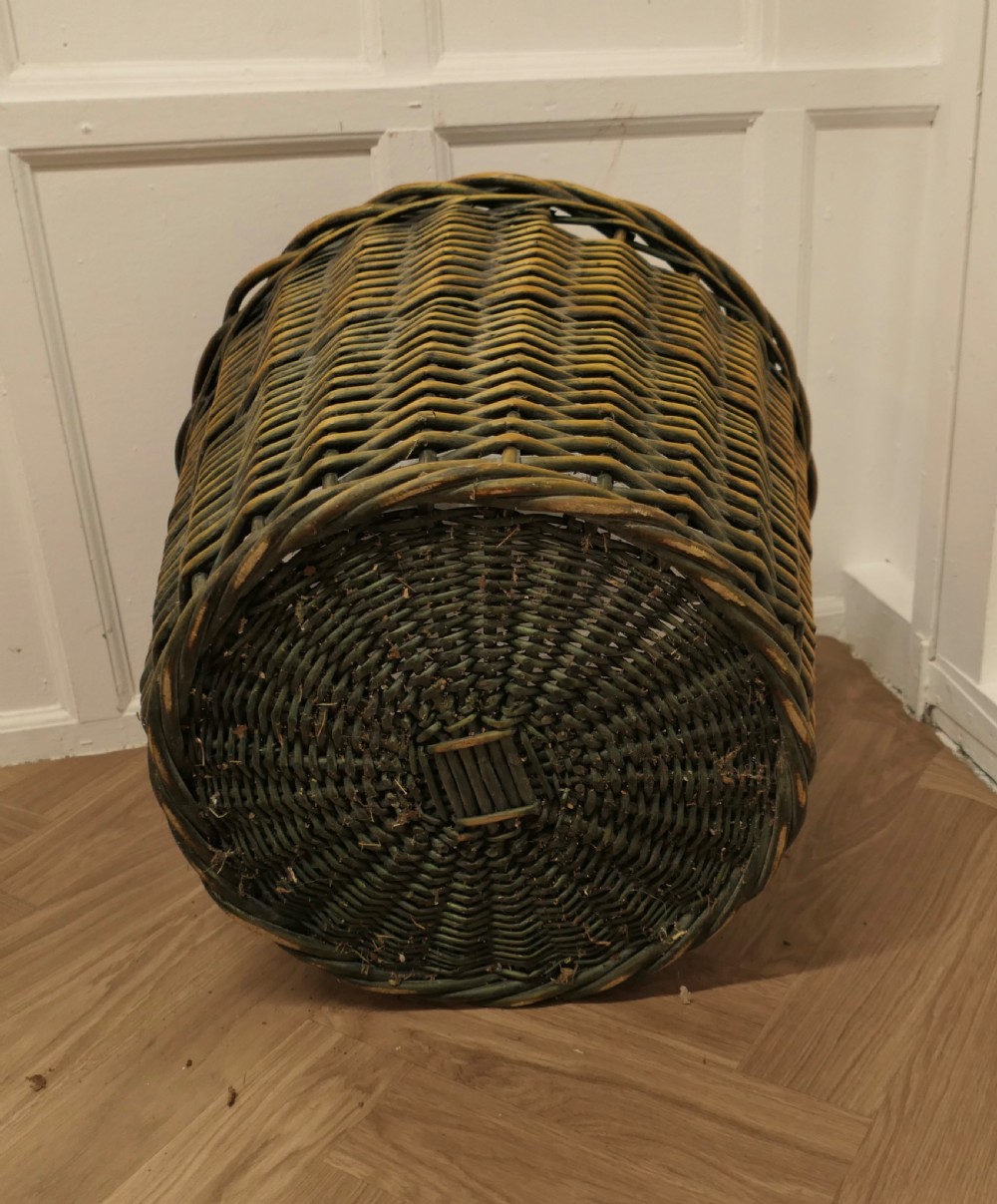 A large circular woven willow log basket with a braided rim resting on a wooden floor. View X