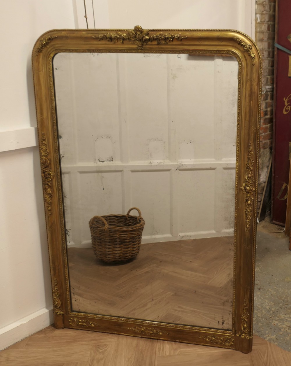 A large 19th-century French Louis Philippe style mirror with a gilded frame featuring rounded top corners and carved floral decoration.