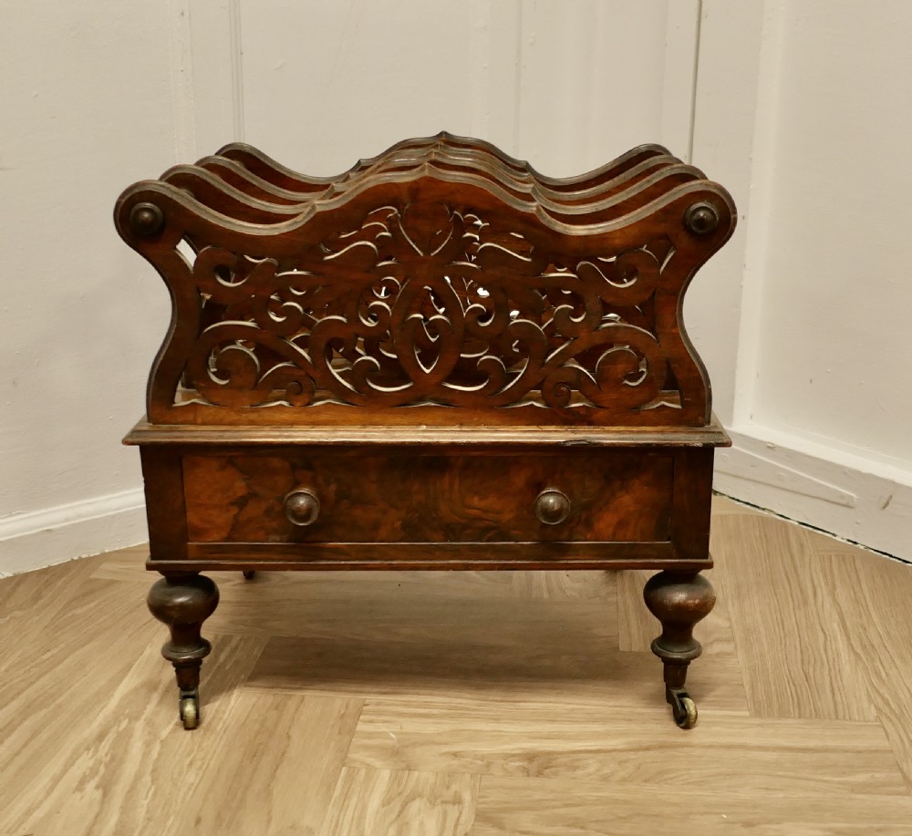 A Victorian walnut Canterbury featuring carved fretwork dividers, a single lower drawer with wooden knobs, turned legs, and brass castors.