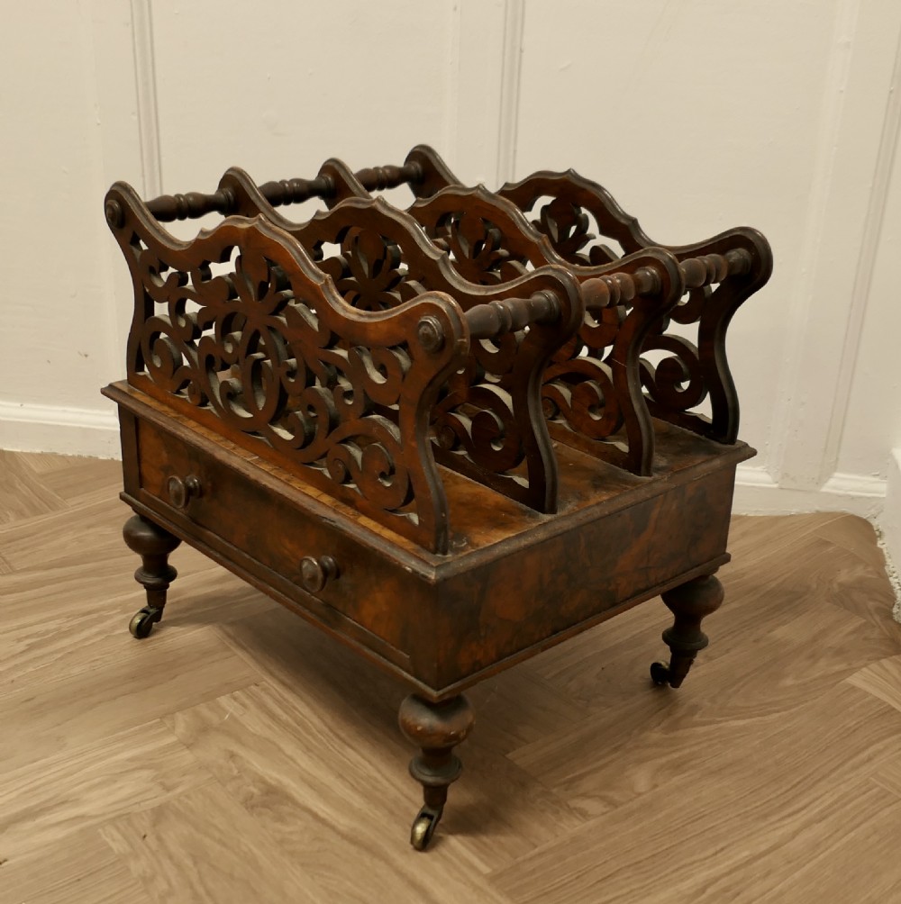 A Victorian walnut Canterbury featuring carved fretwork dividers, a single lower drawer with wooden knobs, turned legs, and brass castors. View III