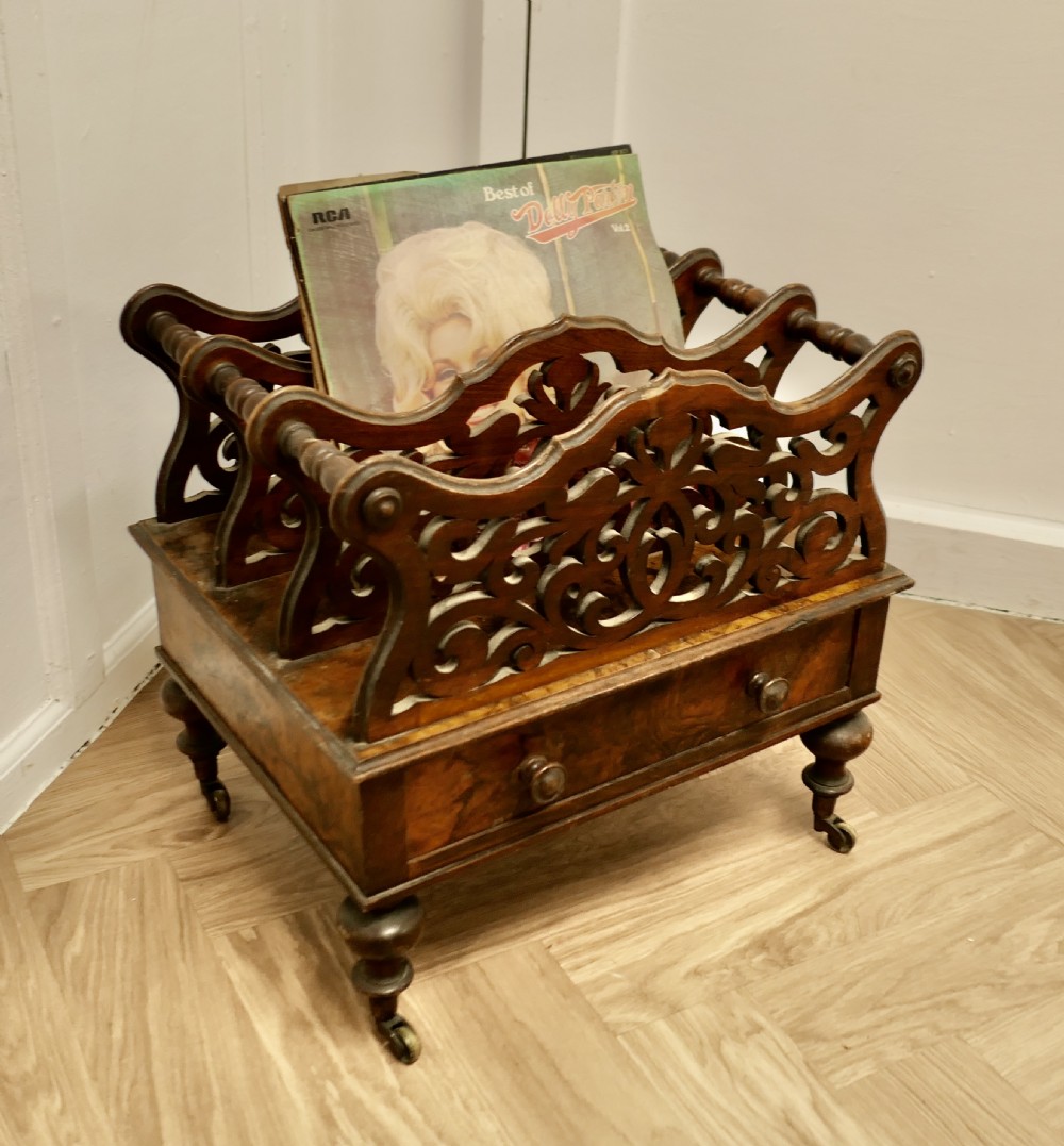 A Victorian walnut Canterbury featuring carved fretwork dividers, a single lower drawer with wooden knobs, turned legs, and brass castors. View V