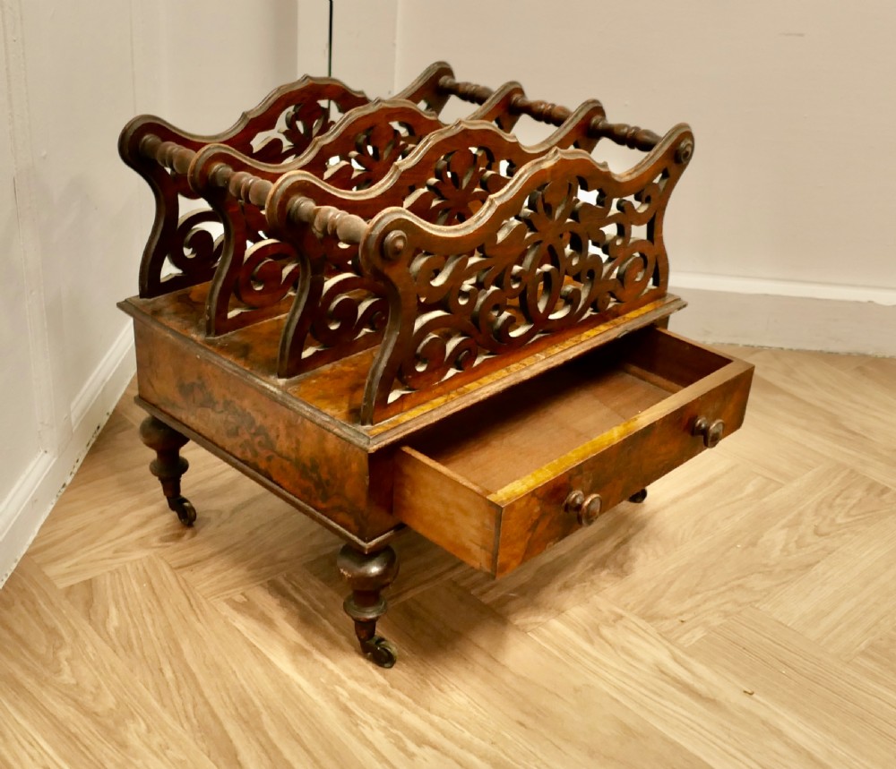 A Victorian walnut Canterbury featuring carved fretwork dividers, a single lower drawer with wooden knobs, turned legs, and brass castors. View VI