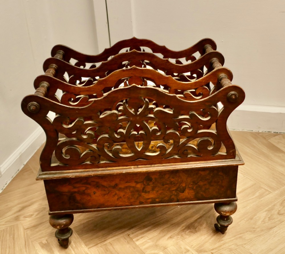 A Victorian walnut Canterbury featuring carved fretwork dividers, a single lower drawer with wooden knobs, turned legs, and brass castors. View VII