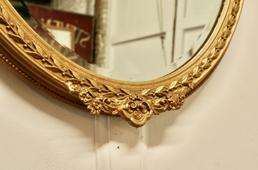 A nineteenth-century French oval wall mirror with an ornate gold leaf frame decorated with leaf motifs and a crest at the top. View III