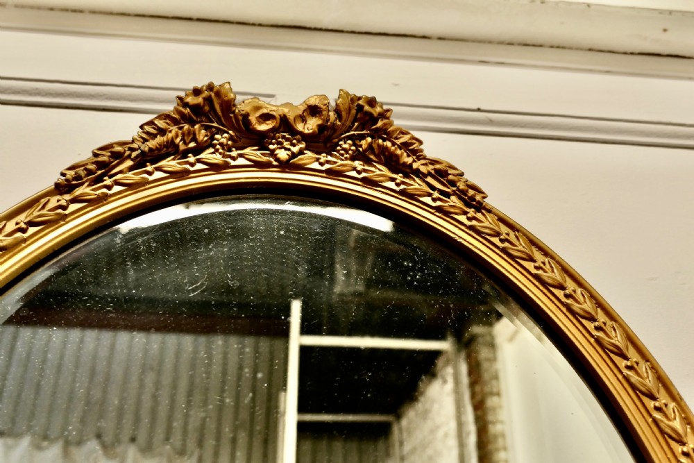 A nineteenth-century French oval wall mirror with an ornate gold leaf frame decorated with leaf motifs and a crest at the top. View V