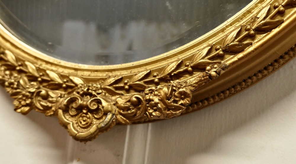 A nineteenth-century French oval wall mirror with an ornate gold leaf frame decorated with leaf motifs and a crest at the top. View VII