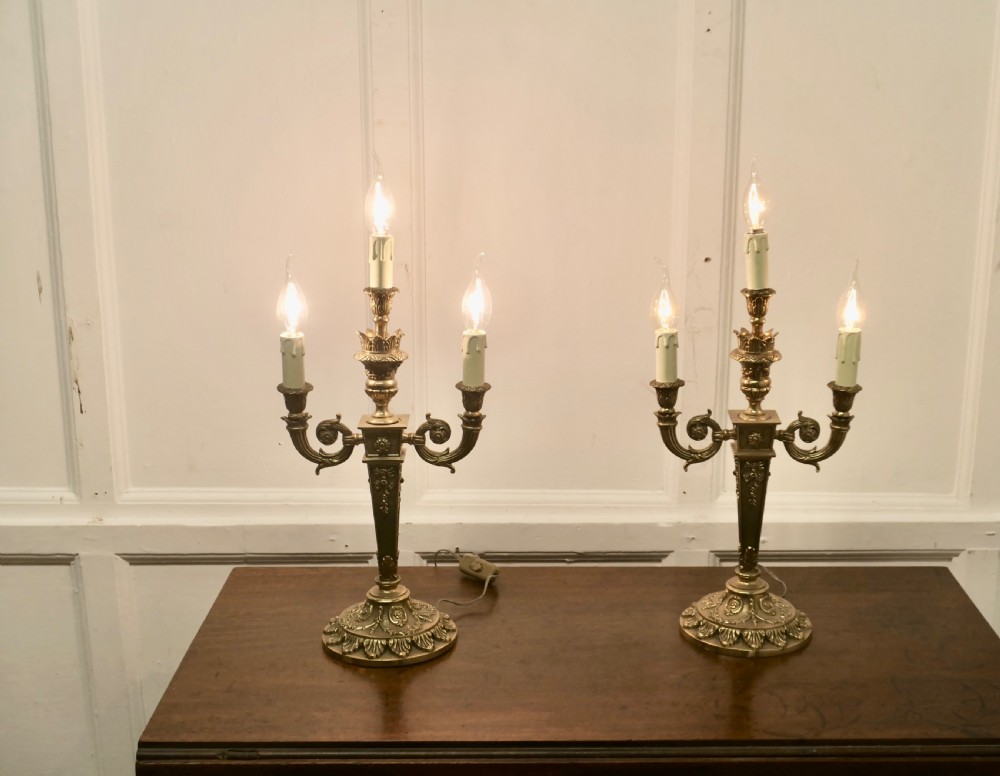 A matching pair of three-branch ornate brass electric candelabra table lamps featuring flame-shaped light bulbs and scrolled arms. View III