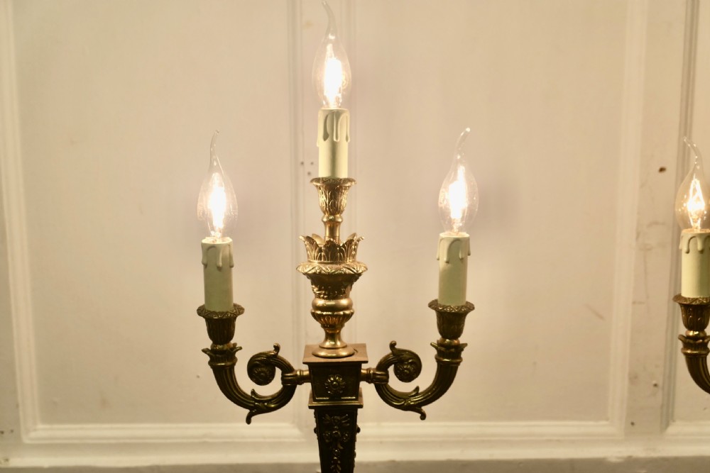 A matching pair of three-branch ornate brass electric candelabra table lamps featuring flame-shaped light bulbs and scrolled arms. View V