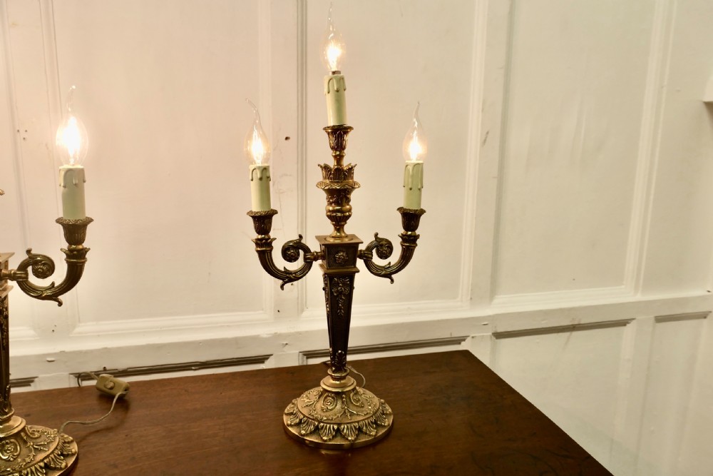 A matching pair of three-branch ornate brass electric candelabra table lamps featuring flame-shaped light bulbs and scrolled arms. View VI