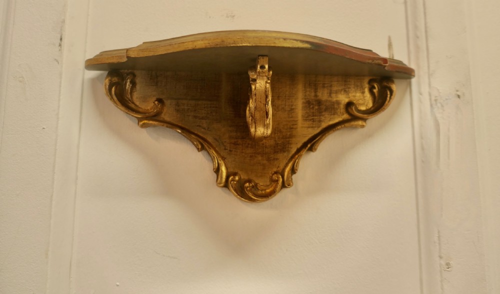 A carved giltwood wall mirror featuring a shell crest hanging directly above a matching gilded wall bracket shelf. View VI