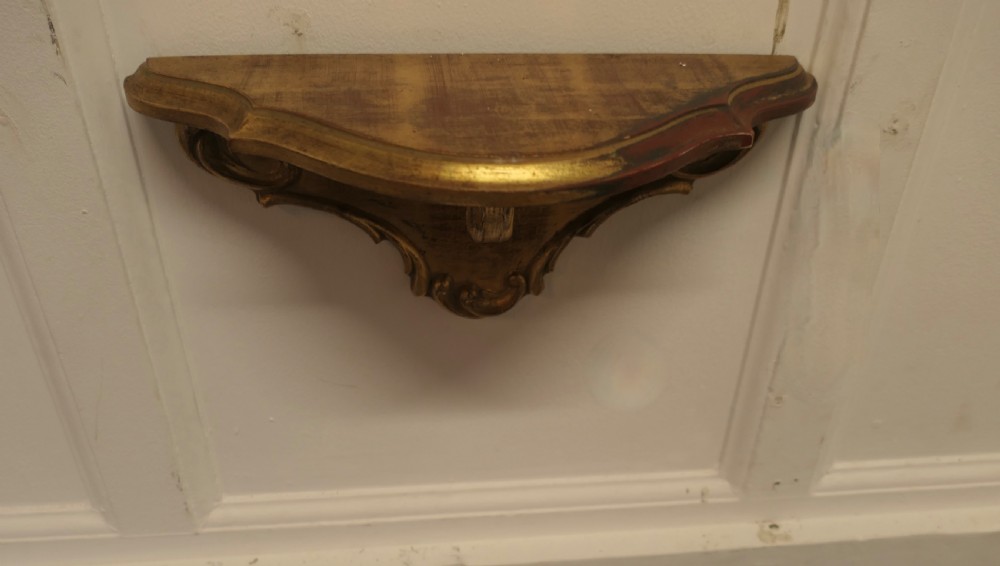 A carved giltwood wall mirror featuring a shell crest hanging directly above a matching gilded wall bracket shelf. View VII