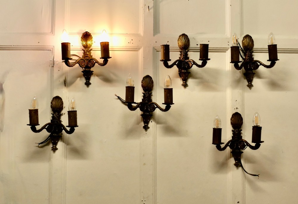 A set of six cast brass twin-branch wall lights featuring scallop shell cresting and twin bulb holders.