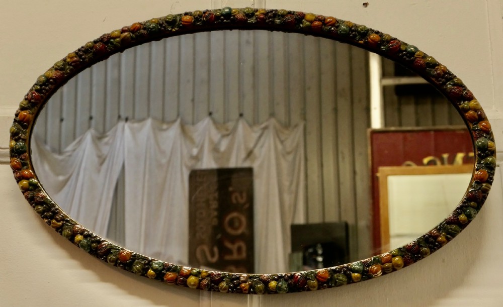A horizontal oval wall mirror featuring a moulded frame encrusted with detailed polychrome fruit and foliage gesso decorations. View II