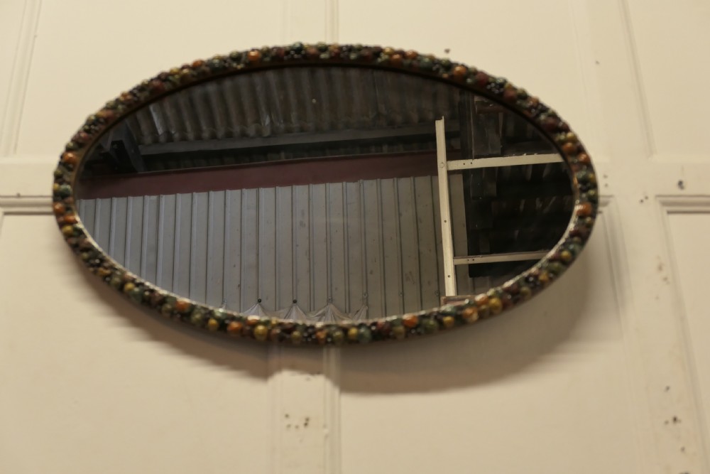 A horizontal oval wall mirror featuring a moulded frame encrusted with detailed polychrome fruit and foliage gesso decorations. View III