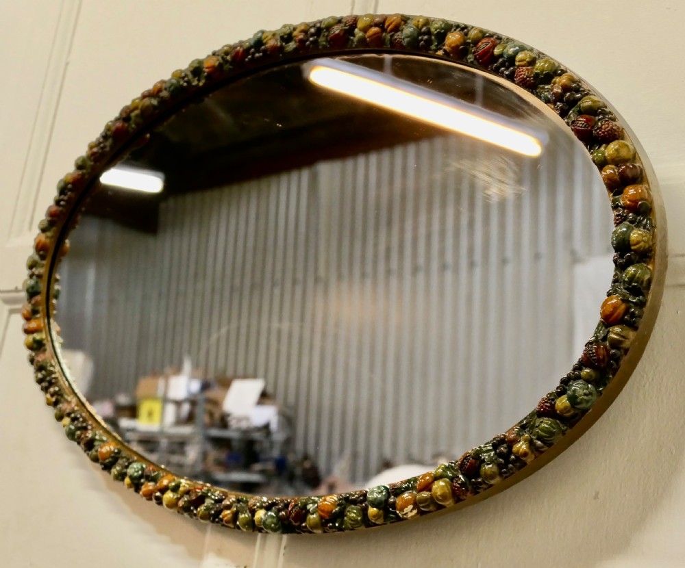 A horizontal oval wall mirror featuring a moulded frame encrusted with detailed polychrome fruit and foliage gesso decorations. View V