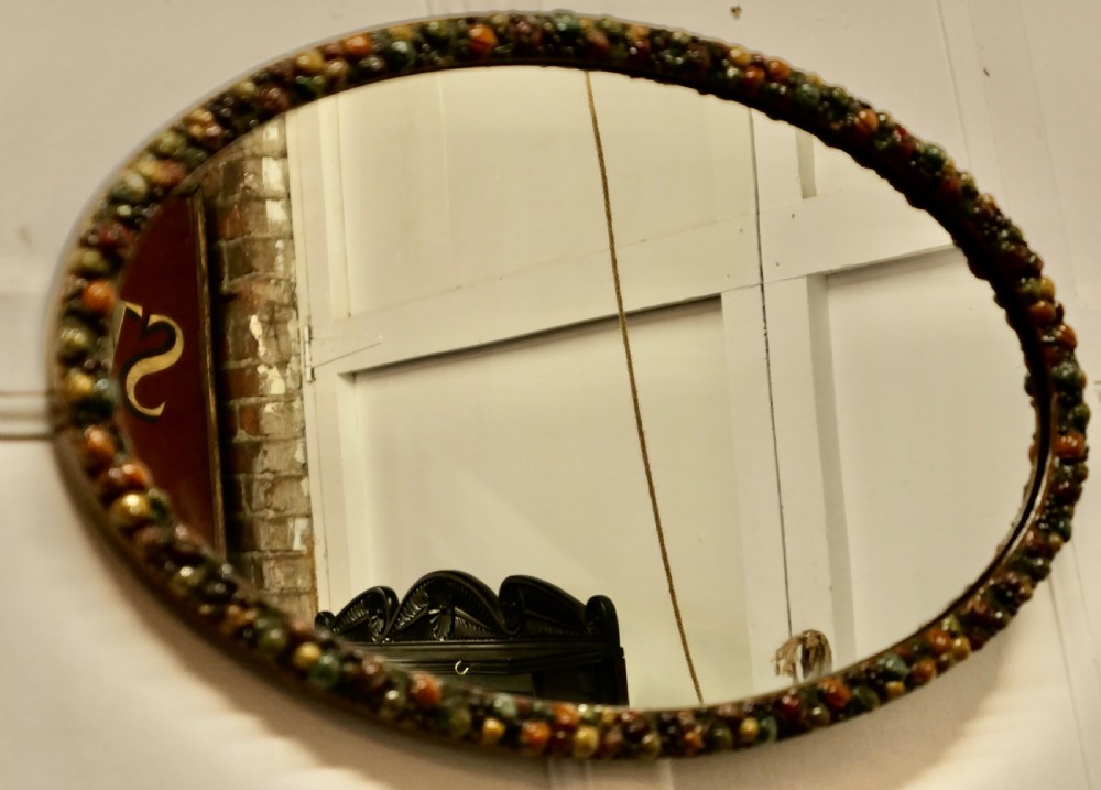 A horizontal oval wall mirror featuring a moulded frame encrusted with detailed polychrome fruit and foliage gesso decorations. View VI