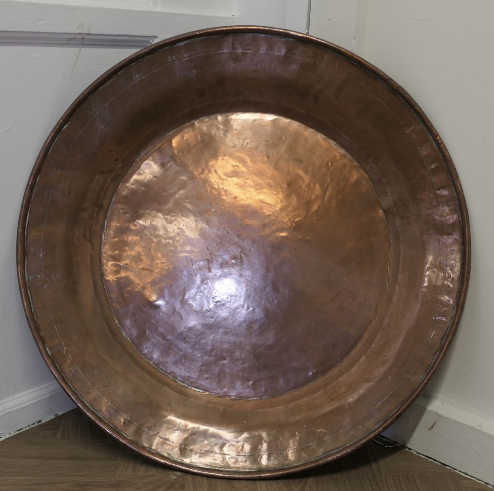 A large round Arts and Crafts hand-hammered copper wall plate displaying a reflective circular central basin and planished rim.