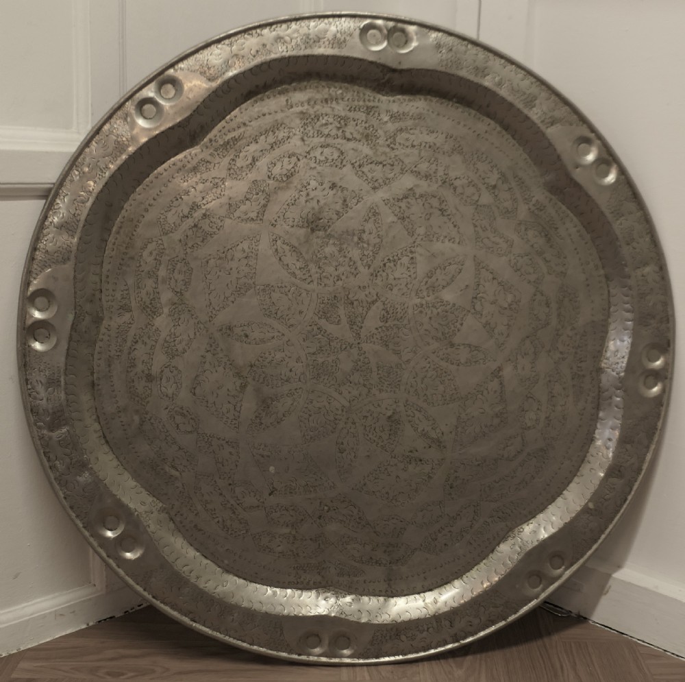 A large circular beaten pewter wall plate featuring intricate hand-hammered geometric engraving with decorative indented rim details.