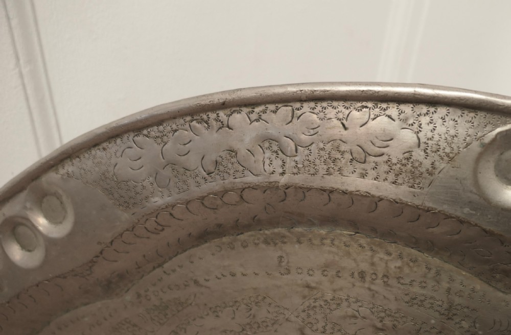 A large circular beaten pewter wall plate featuring intricate hand-hammered geometric engraving with decorative indented rim details. View V