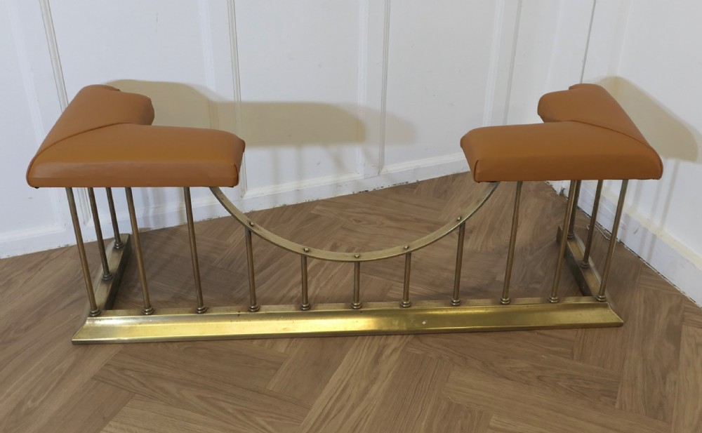 A brass club fender featuring twin tan leather upholstered corner seats supported by vertical brass spindles on a moulded base. View II