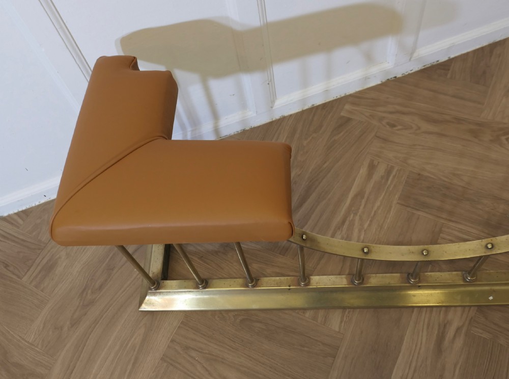 A brass club fender featuring twin tan leather upholstered corner seats supported by vertical brass spindles on a moulded base. View III