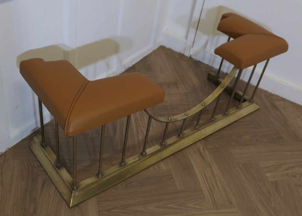 A brass club fender featuring twin tan leather upholstered corner seats supported by vertical brass spindles on a moulded base. View V