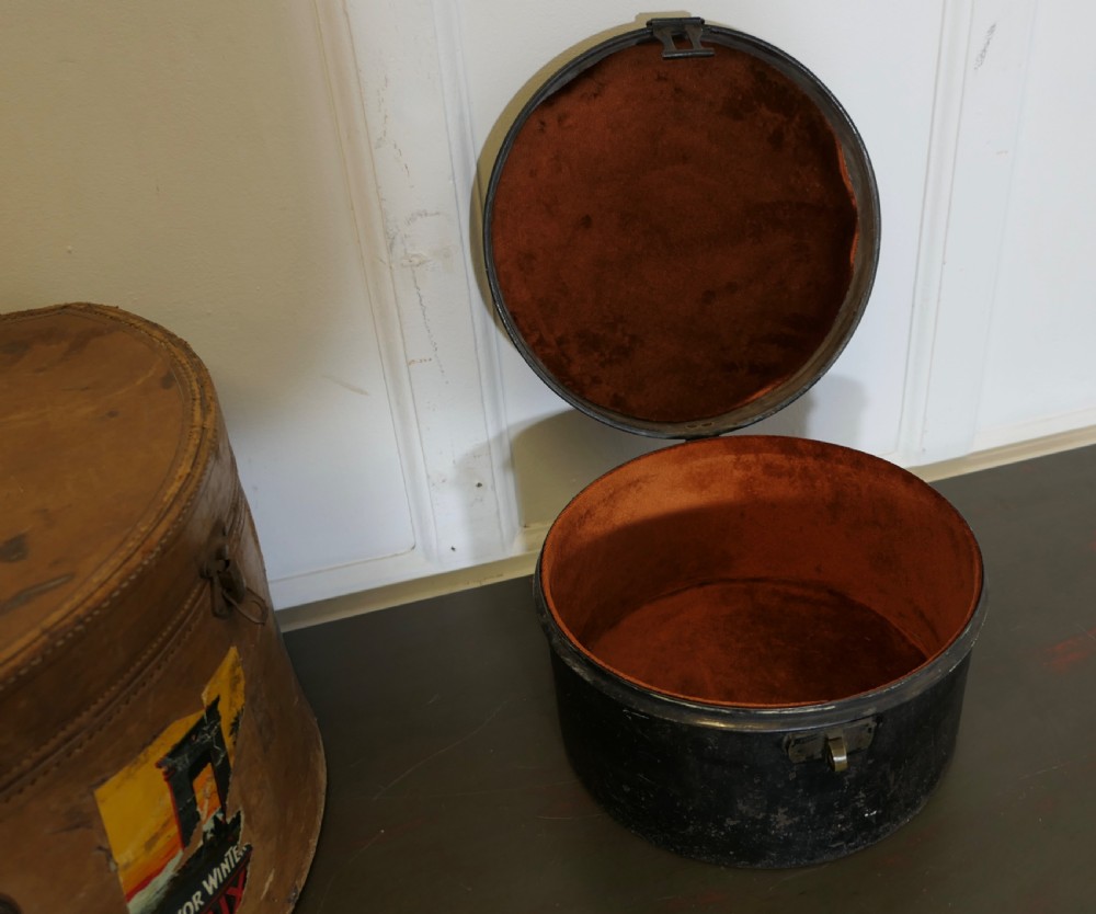 A nineteenth-century tan leather hat box featuring travel stickers and a leather handle, topped with a smaller black metal hat case. View VII