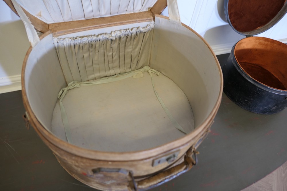 A nineteenth-century tan leather hat box featuring travel stickers and a leather handle, topped with a smaller black metal hat case. View VIII
