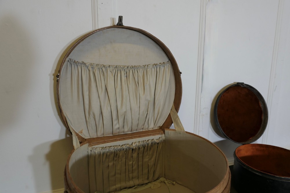 A nineteenth-century tan leather hat box featuring travel stickers and a leather handle, topped with a smaller black metal hat case. View XI