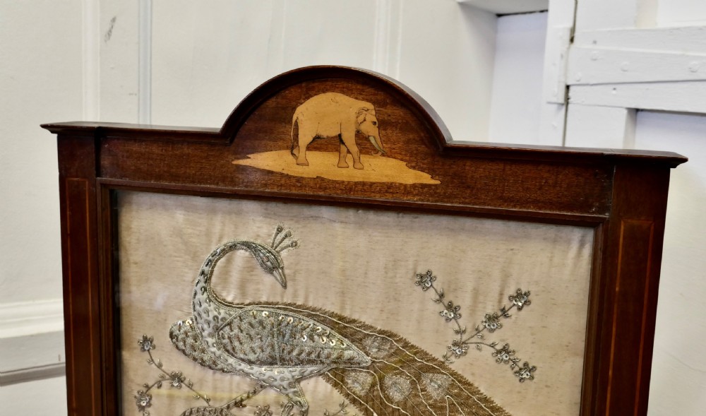 A dark wood framed standing fire screen displaying metallic embroidery of two peacocks and the Taj Mahal. View III