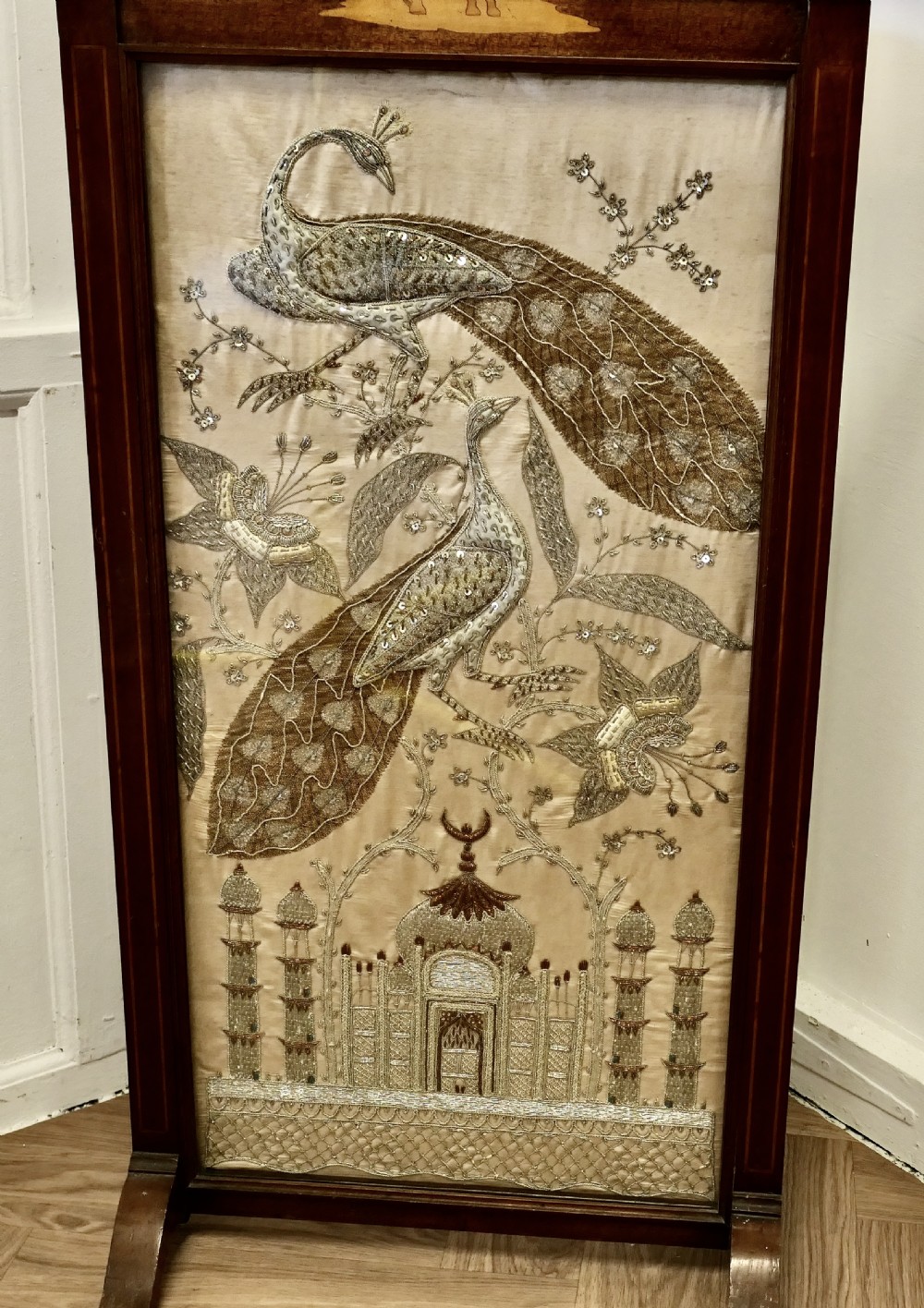 A dark wood framed standing fire screen displaying metallic embroidery of two peacocks and the Taj Mahal. View V