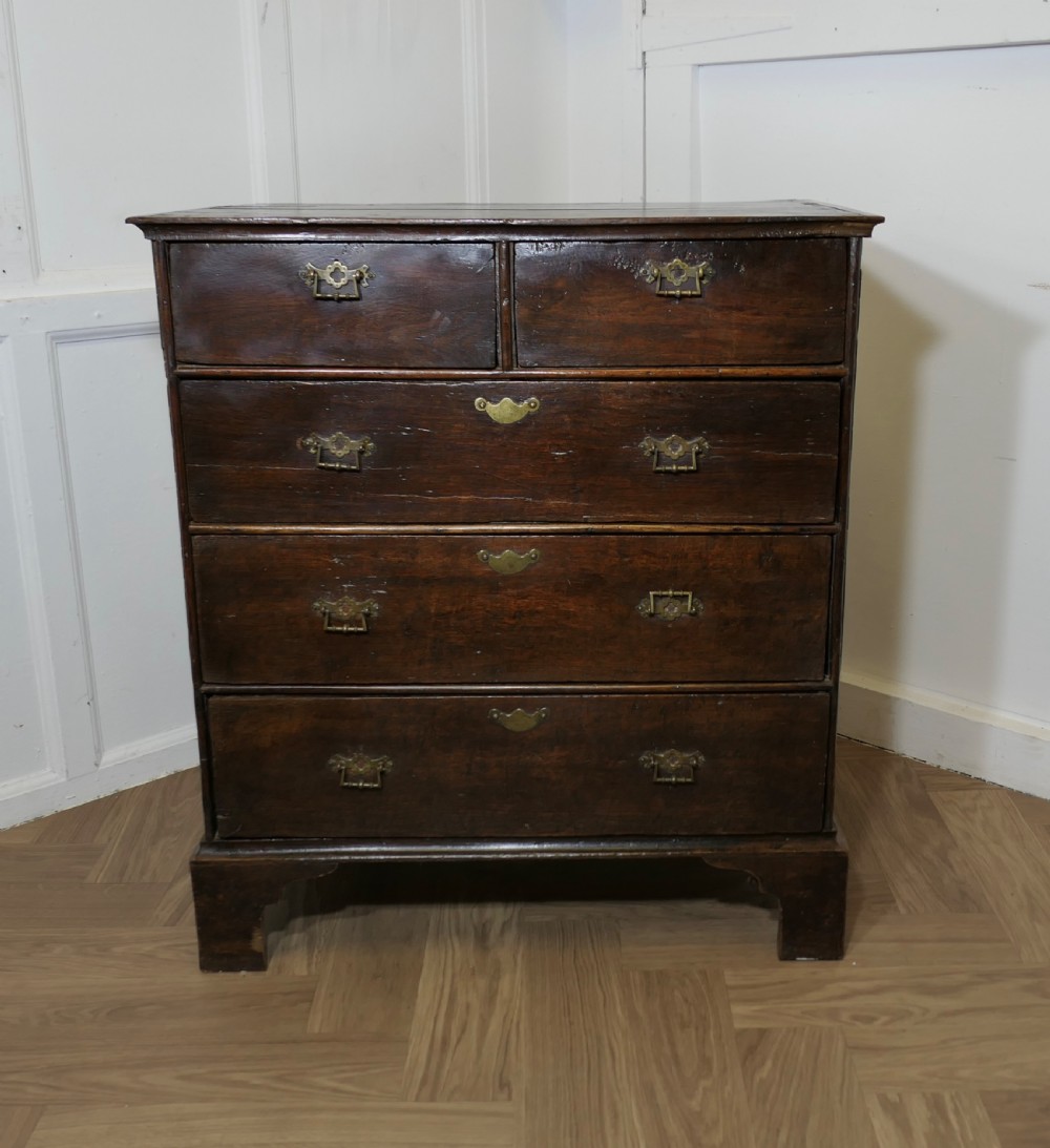 An 18th-century dark oak chest of drawers featuring two short drawers over three long drawers with brass handles and bracket feet.