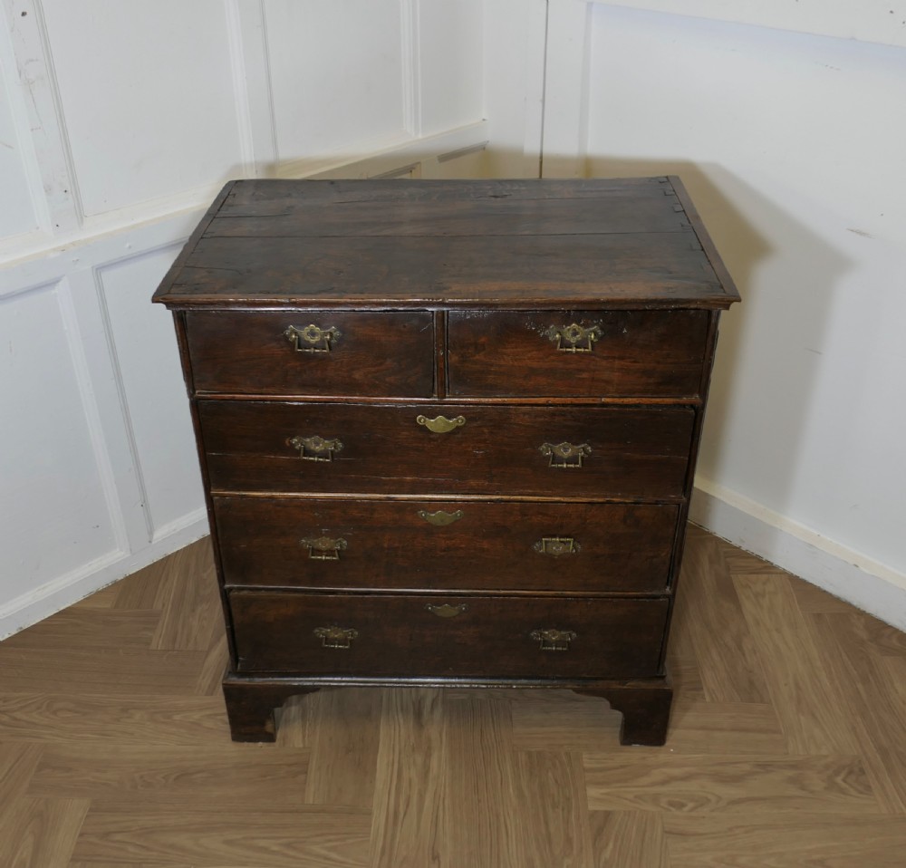 An 18th-century dark oak chest of drawers featuring two short drawers over three long drawers with brass handles and bracket feet. View II
