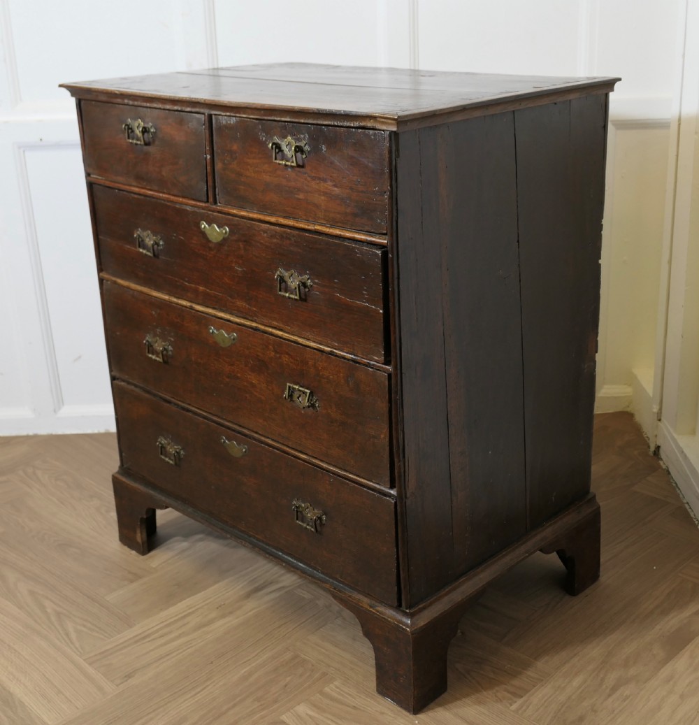 An 18th-century dark oak chest of drawers featuring two short drawers over three long drawers with brass handles and bracket feet. View III