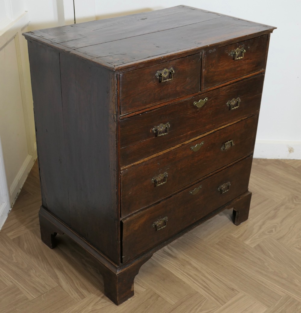 An 18th-century dark oak chest of drawers featuring two short drawers over three long drawers with brass handles and bracket feet. View V