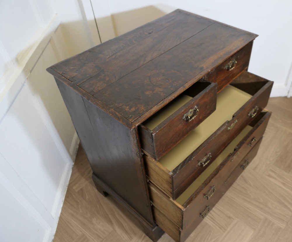 An 18th-century dark oak chest of drawers featuring two short drawers over three long drawers with brass handles and bracket feet. View VI