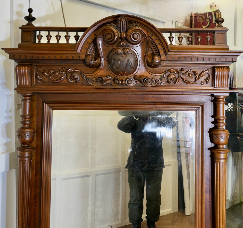 A large dark timber French wall mirror featuring a carved central crest, top balustrade gallery, and side fluted columns. View IV