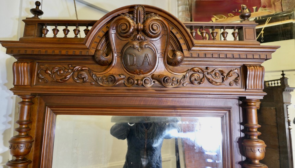 A large dark timber French wall mirror featuring a carved central crest, top balustrade gallery, and side fluted columns. View VI