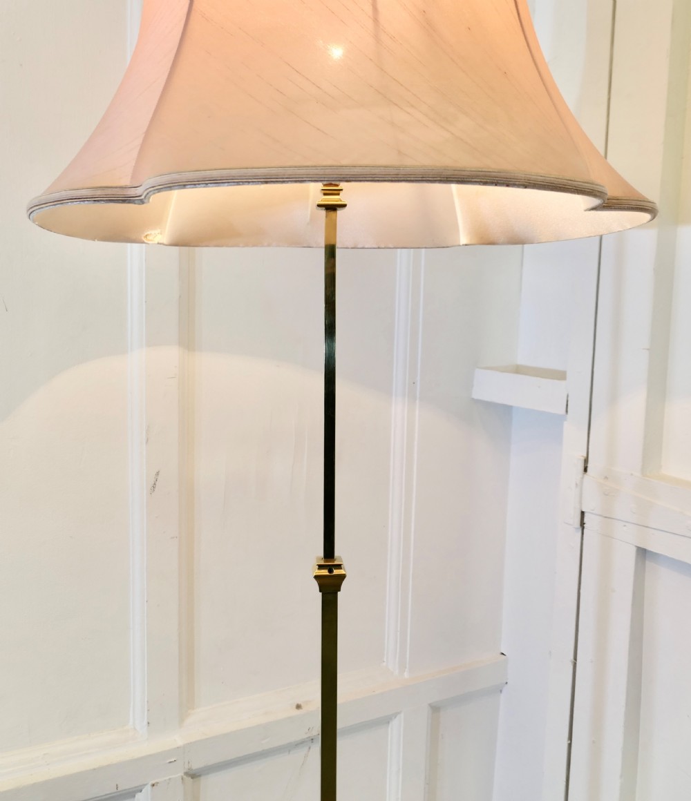 An Arts and Crafts brass standard floor lamp featuring a tapered column, splayed tripod feet, and a flared light pink shade. View III