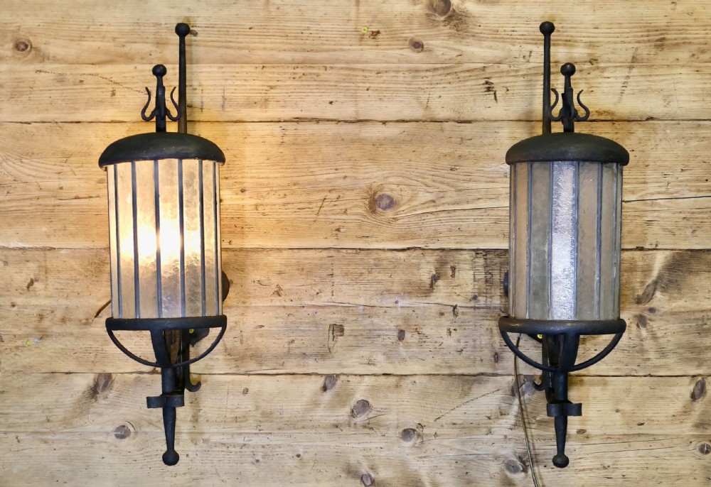 A pair of large black wrought iron wall lanterns featuring cylindrical glass shades with vertical metal bars and decorative finials at the top and bottom.